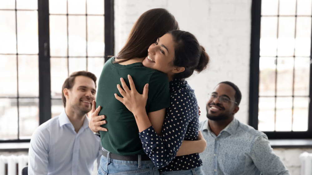 Woman hugging each other with their happy male friends