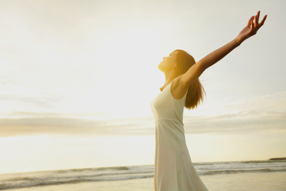 A woman in white dress who is very happy by the beach