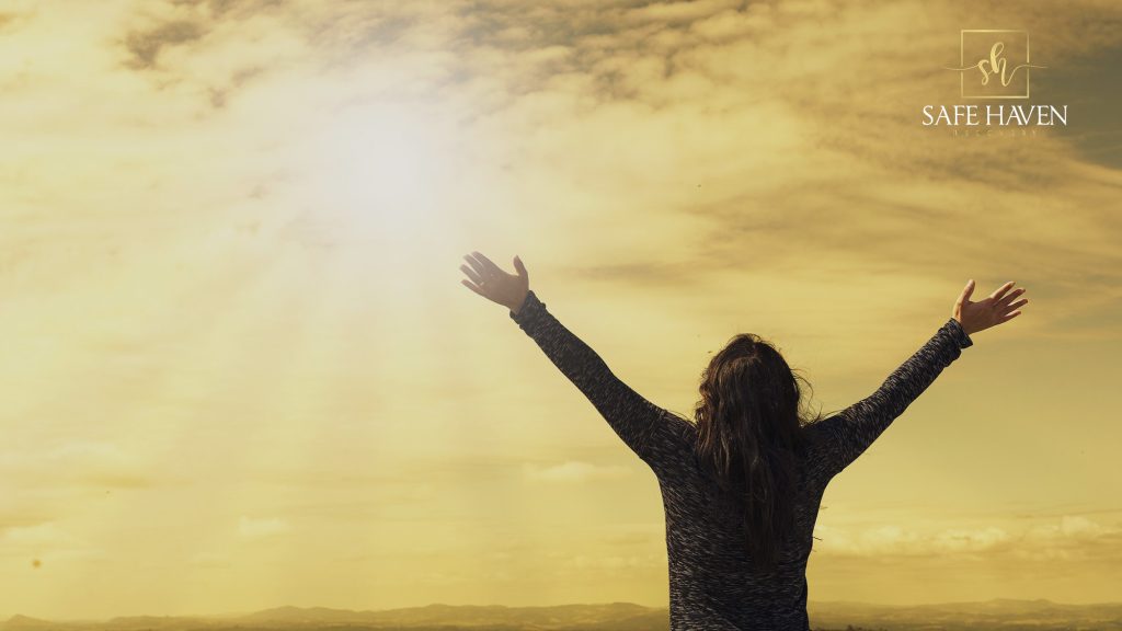 Woman raising both of her arms under the sun