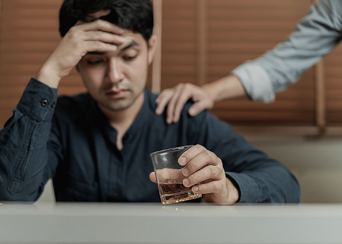 a guy holding his head holding a glass of alcohol