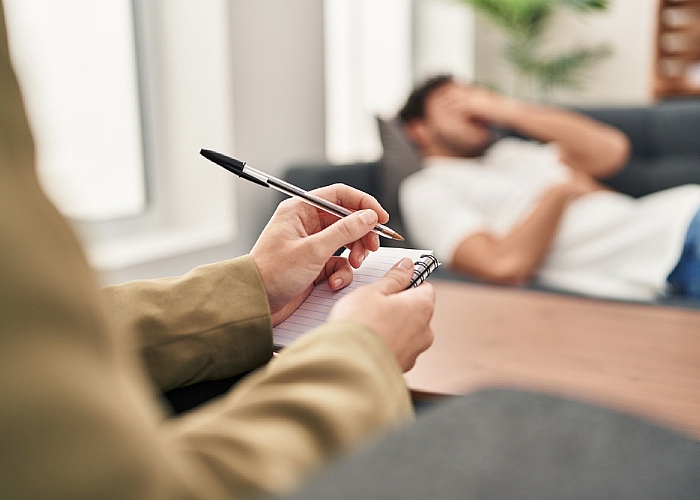 A man lying in a couch while therapist writing something