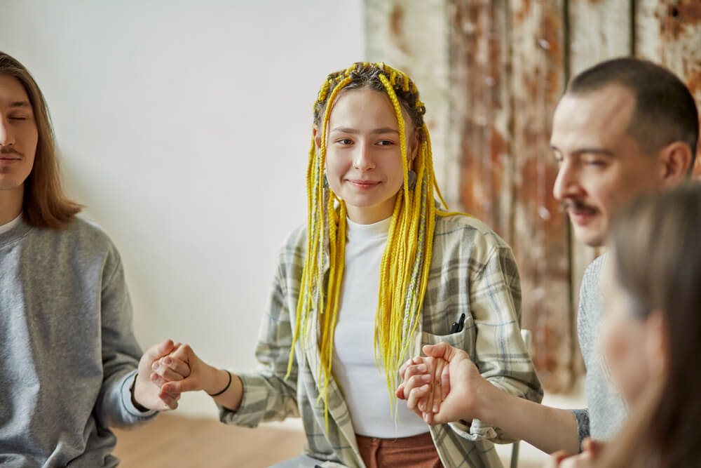 Woman with braided yellow hair holding hands with her fellow patients