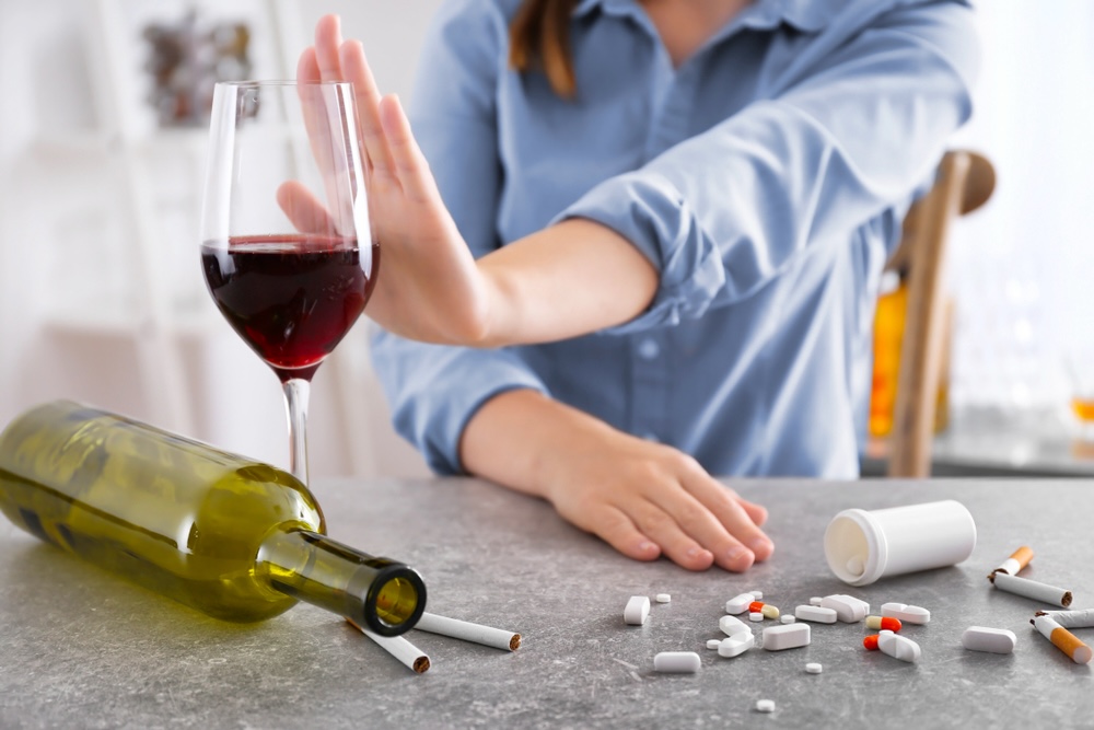 Young woman refusing glass of wine and drugs while sitting at table