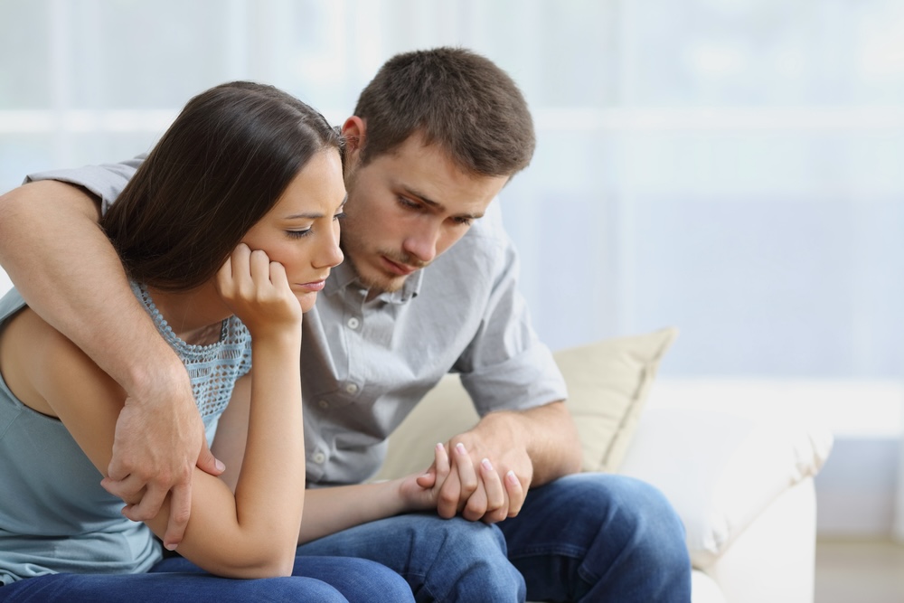 Sad couple comforting each other sitting on a couch