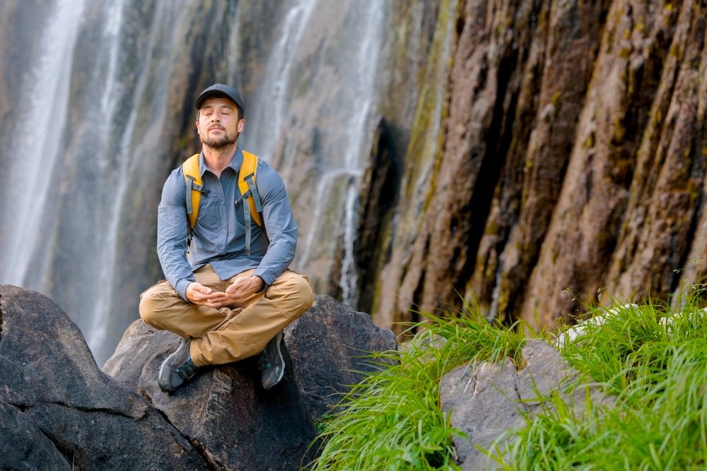 A man meditating while sitting on a big stone