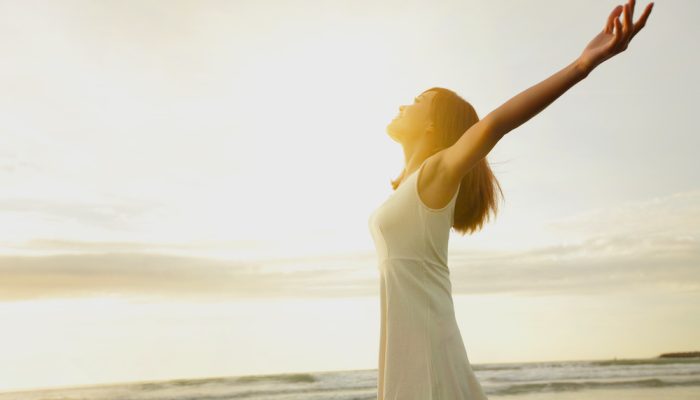 A woman in white dress who is very happy by the beach