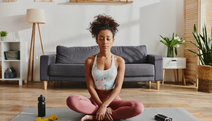 A woman in activewear suffering from substance abuse practicing yoga on a mat in a cozy living room setting