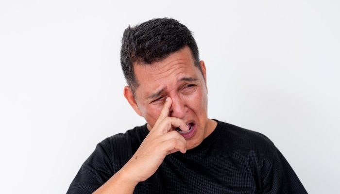 A man in black shirt removing eye discharge from his tear duct.