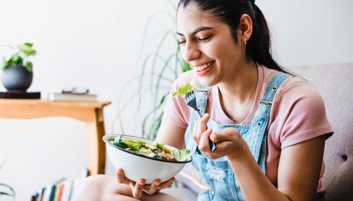 A woman sitting on a couch while eating salad